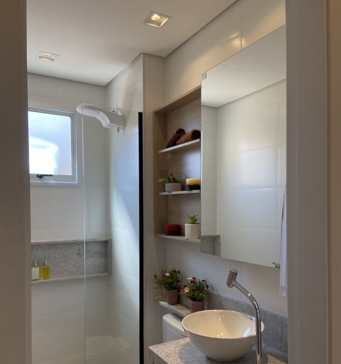 Banheiro compacto decorado com prateleiras e vasos, destacando soluções inteligentes para quem busca praticidade e estilo. Banheiro com prateleiras de madeira e vasos decorativos próximos ao espelho.