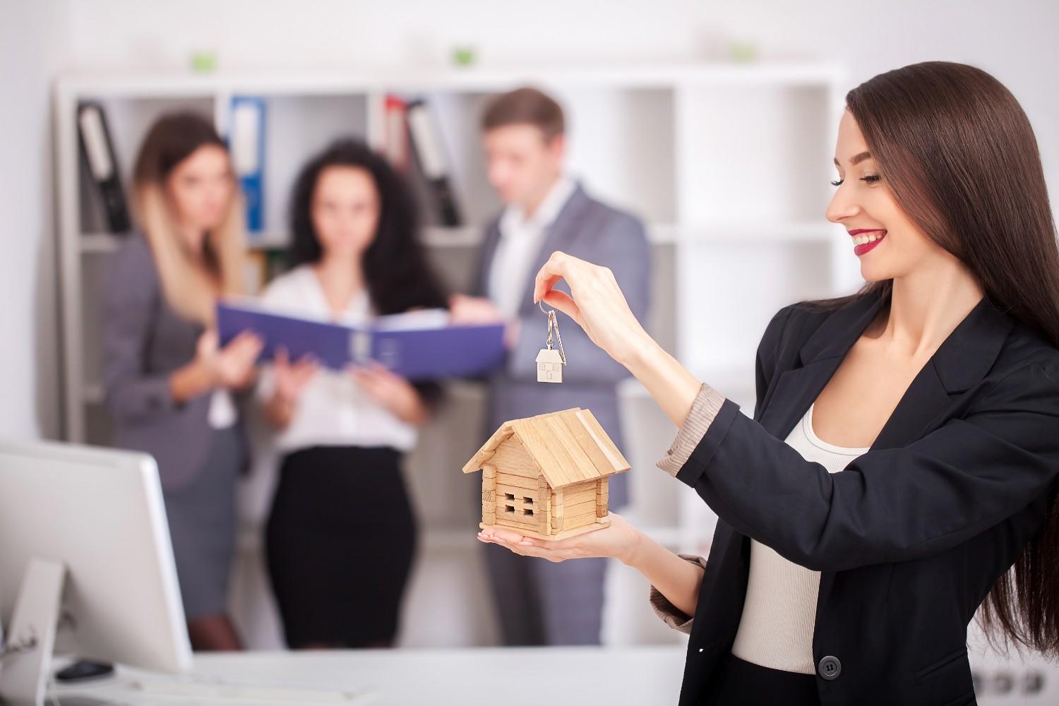 Mulher sorridente segurando uma chave e uma maquete de casa, simbolizando a conquista do primeiro imóvel em promoção.